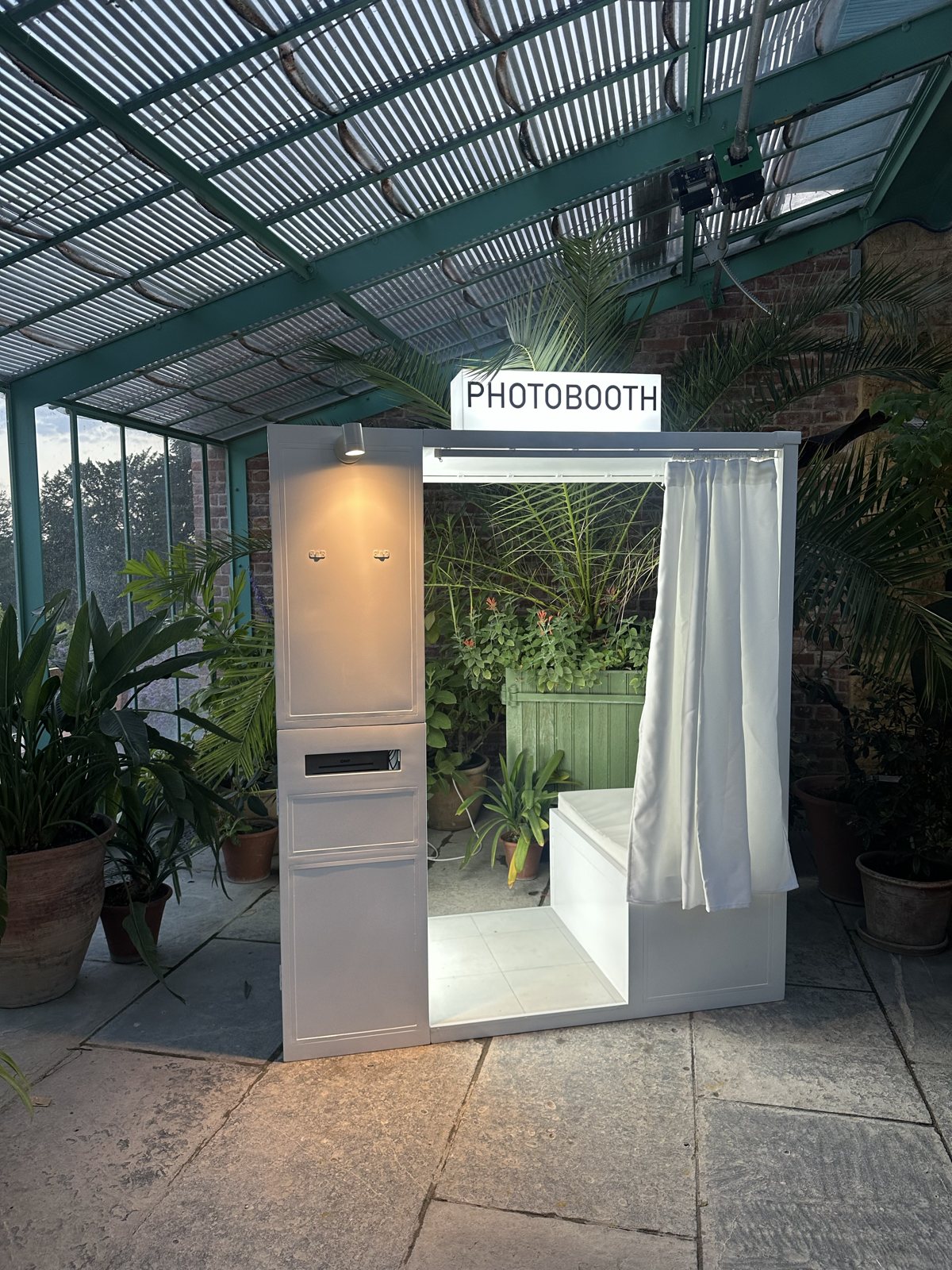 The white enclosed photo booth in a glasshouse surrounded by palms